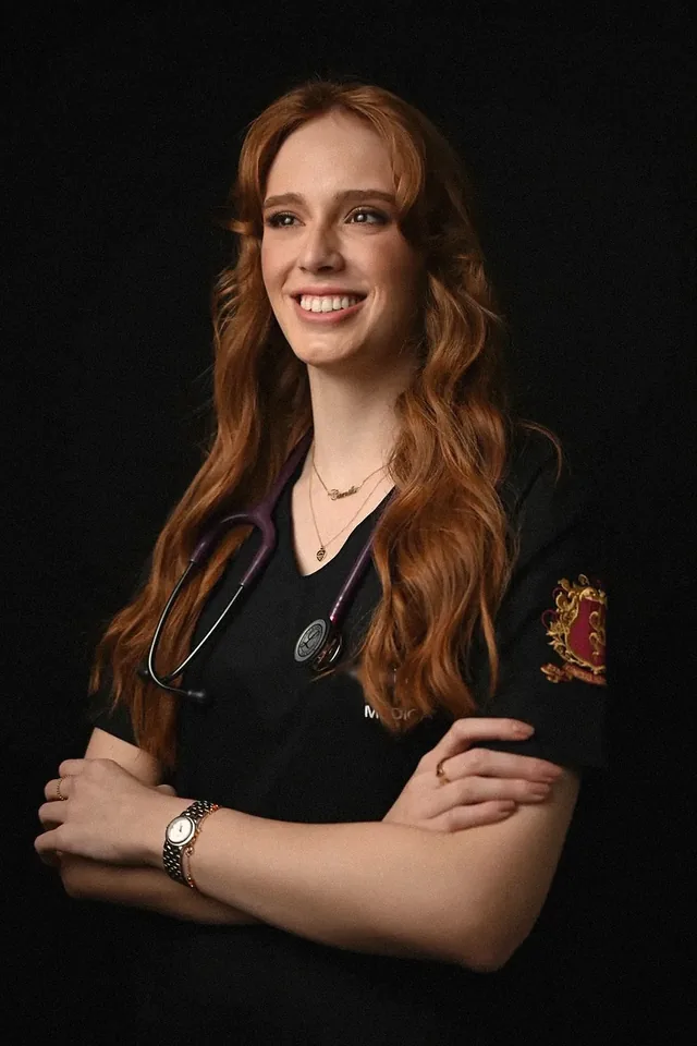Dra. Camilla Vicelli de braços cruzados, com roupa cirúrgica preta e estetoscópio no pescoço